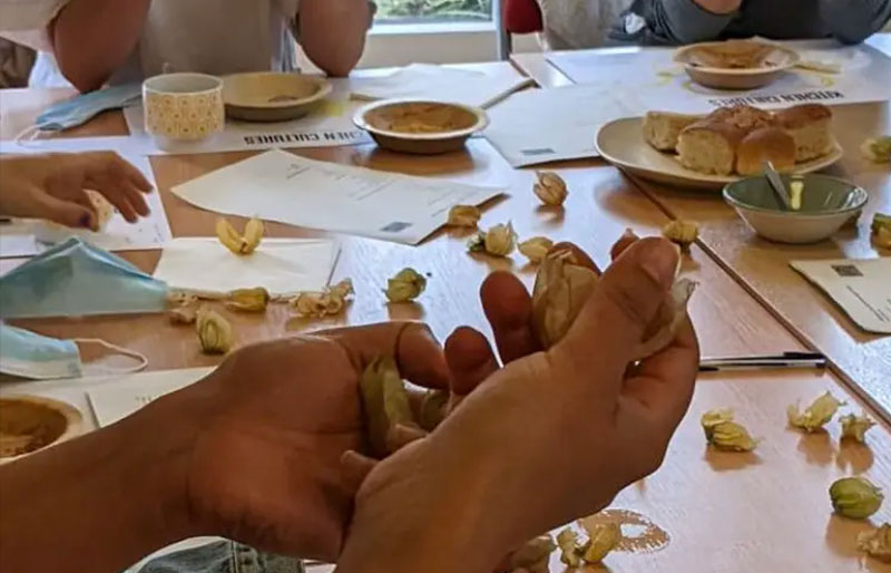 A pair of hands at a table, holding something while people gather round a table
